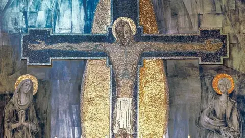 Jesus is depicted with a golden halo with his arms stretched and pinned to the cross with Mary and St John - also with golden halos - praying on both sides. The cross is surrounded by a dazzling golden oval.