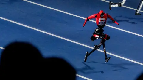 A red humanoid robot runs on a racing track.