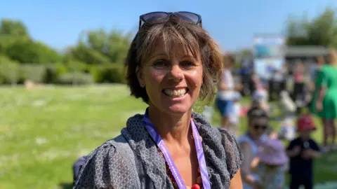 Sharon Gill stood in a field. She is smiling and wearing a blue top. She has medium length brown hair.
