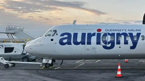 Aurigny plane - blue text and white plane. Orange and white cone on a runway with the plane