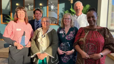Jon Wright/BBC Six people pose holding trophies inside a cafe building