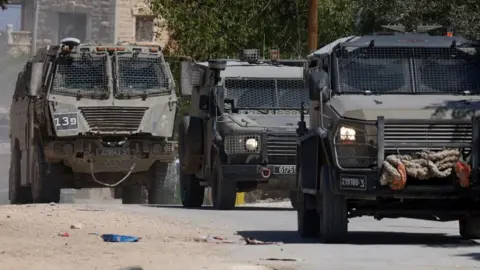 EPA Three armoured Israeli miltiary vehicles drive on a road in Jenin