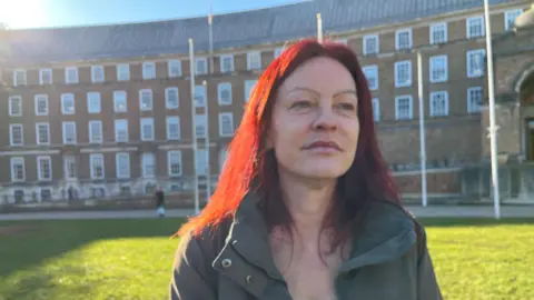 Claire Cavanagh This is a picture of Christine Townsend, Green party councillor and Chair of the Children and Young People Committee on Bristol City Council standing in front of City Hall in Bristol on a sunny day wearing an anorak and white top