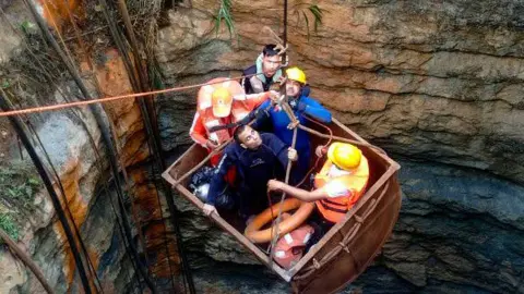 The image shows divers wearing protective helmets and jackets entering a coal mine using a pulley, to rescue trapped miners in Umrangso, in the Dima Hasao district of India's Assam state on January 7, 2025. 