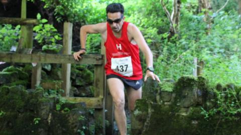 A man wearing a red running vest jumping through a stile