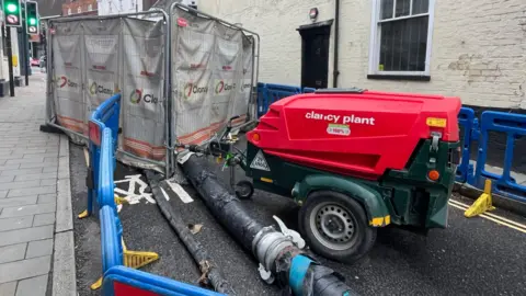 Machines and fences surrounding the sinkhole in Dorking, with a pipe on the floor