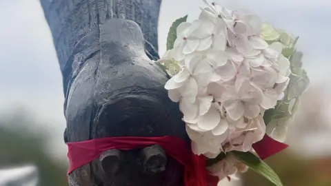 Andy Roberts/BBC A white flower is tied to the boot of the John Atyeo statue at Ashton Gate in memory of Liam Manning's baby son Theo who has died