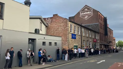 Chloe Aslett/BBC Long queue of people outside The Leadmill building, with "The Leadmill" sign above them, painted on the side of a redbrick building.