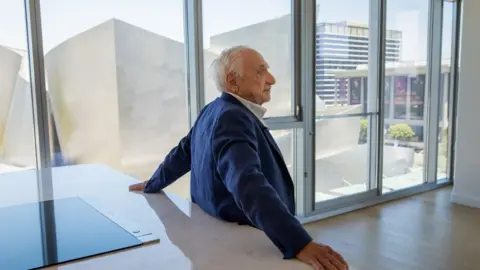 Jay L. Clendenin / Los Angeles Times via Getty Images Frank Gehry has his back to the camera as he stands at a kitchen island within his personal apartment at  The Grand by Gehry development in Los Angeles