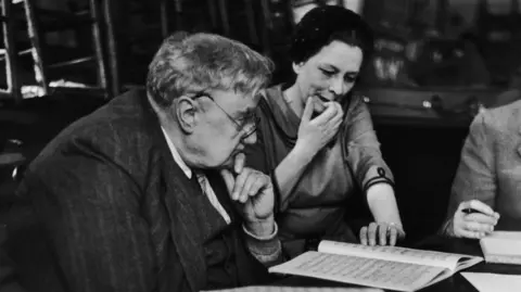 Getty Images Black and white photo of composer Ralph Vaughan Williams studying a song sheet with a woman sat next to him also looking at the sheet