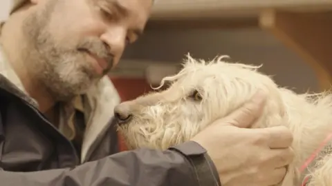 Dogspiracy TV vet and animal welfare campaigner Dr Marc Abraham OBE petting a white dog in a still of his documentary Dogspiracy.