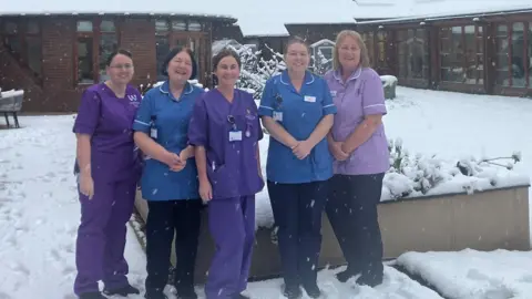 Nightingale House Hospice Five women, all dressed in nursing uniforms. stand in the snow covered courtyard of Nightingale House Hospice