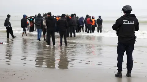 A police officer looks out to sea as a group of people wearing inflatable jackets stand in shallow water in Gravelines earlier this month.