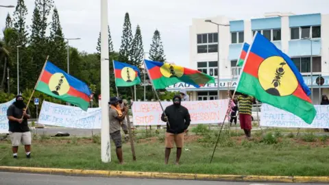  Delphine MAYEUR / AFP Pro-independence supporters hold flags of the Kanak and Socialist National Liberation Front (FLNKS) during a rally in support of the independentists who were arrested, in Noumea on June 22, 2024