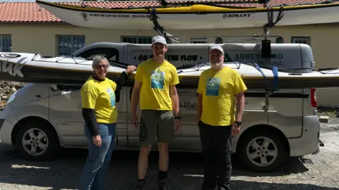 Brad, his mum, and his coach stand in front of the kayak that will take them to Lundy.
