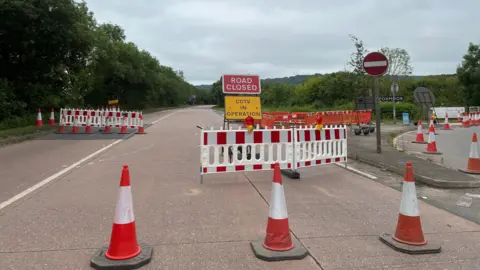 The picture shows an empty link road. There are three cones in the road and signs saying "Road closed".