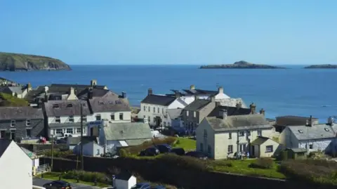 Getty Images A view of houses against a backdrop of the sea. A set of houses, some detached.  A cliff head can be seen in the background.