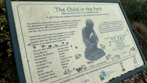 Elliot Deady/BBC A sign in a park with the heading "The Child in the Park - Billericay Early Years Forum Millennium Project". It says: "The statue is a permanent symbol for Billericay to commemorate the Millennium. It provides a vision and hope for the future, celebrating the child, the importance of life-long learning, and the care of our environment for future generations."