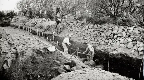 Scilly Arts and Heritage A Victorian era picture shows a group of men digging a large grave with pickaxes. It's in the St Mary's Old Town Church on The Isles of Scilly