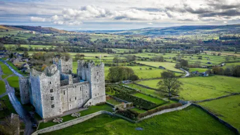 Getty Images An aerial view of a large, medieval stone castle set within a broad, green rural landscape. Beyond the castle, the view opens out into rolling countryside.