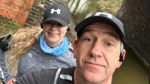 Mark Barrett A man and woman, both in exercise clothing, and wearing black caps, look to the camera. There is a canal to the side of them