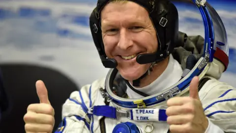 Tim Peake in astronaut gear smiles to the camera with his thumbs up.