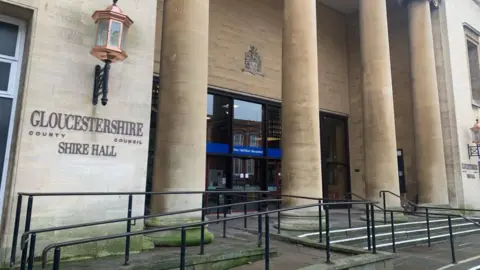 LDRS The entrance to Gloucestershire County Council's Shire Hall. It is a large building with steps and four tall stone columns in front of the main doors.