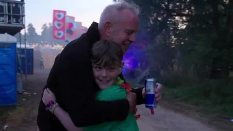 Rob Williams A man with grey hair and black jacket hugs a young boy with brown hair and green T-shirt.