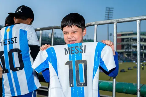 Getty Images A fan holds a jersey of Argentine footballer Lionel Messi and poses for a photo at Arun Jaitley Cricket Stadium during the Lionel Messi G.O.A.T Tour on December 15, 2025 in Delhi, India