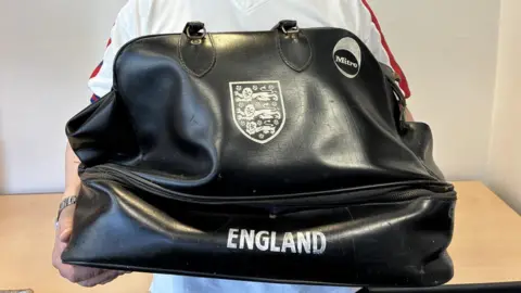 An old black football kit bag held up to the camera