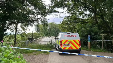 Jacob Tomlinson/BBC Police van in front of bridge with police tape behind it