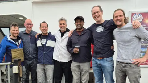 Image shows the chain ferry challengers along with Dan Dimissie and one friend who couldn't participate. They are all huddled together 