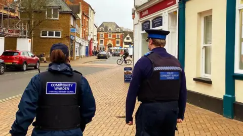 Two council community wardens walking through Banbury market place.