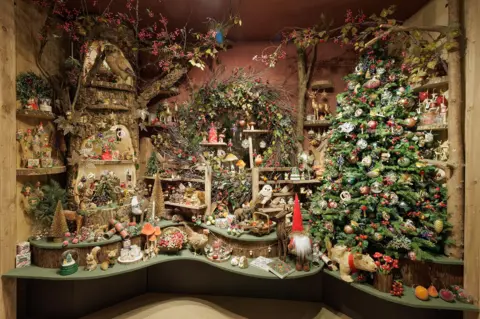 Gisela Graham London Display of Christmas decorations and wreaths with a tree trunk used to show them and a Christmas tree