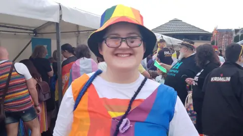 Jackson smiling into the camera wearing a rainbow hat and top. People milling about in background