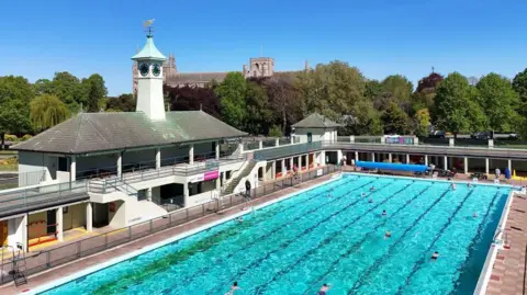People swimming at Peterborough Lido, an outdoor pool with blue water in the centre of Peterborough.