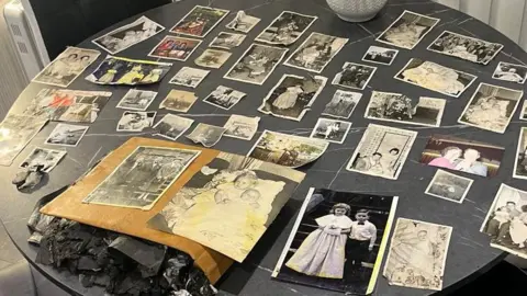 William Lindsay Family photos are spread out across a kitchen table, showing black and white images of children and families as well as a few colour images.