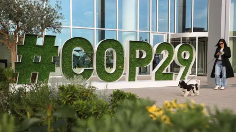 Reuters A woman with a dog walks past a sign saying #COP29