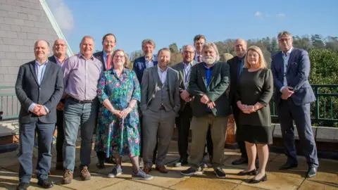 Winchester City Council A 'team,' photo of 13 council leaders posing on a terrace with trees in the background