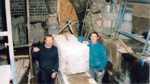 Hebden Bridge Mill Two men stand next to some stone blocks as they make a waterwheel in a mill in Hebden Bridge