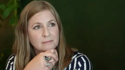 Kate Parrinder has long brown hair and is wearing a dark blue and white stripy top.