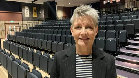 Estelle Rowe, a woman with short grey hair The image is taken inside the auditorium at Heywood Civic. 
