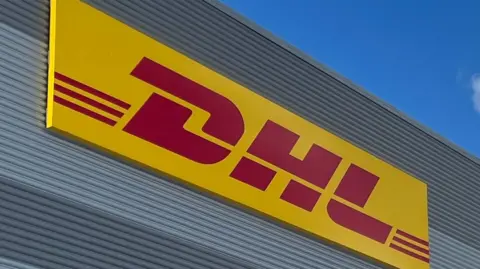 A yellow and red DHL logo fixed to the side of a warehouse.