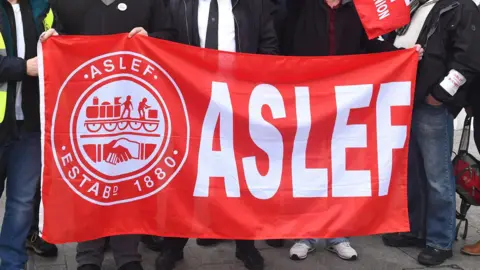 PA Media A close up shot of five people holding up a red rectangular banner reading: Aslef with an Aslef logo on the left.