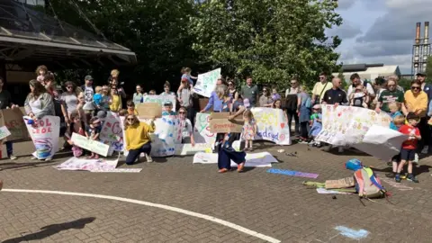 This image shows a large outdoor gathering of people, including many adults and children, assembled on a paved area outside County Hall in Cardiff. The group is posing together, facing the camera, and many are holding handmade banners and signs calling for the establishment of a Welsh-medium secondary school in south Cardiff