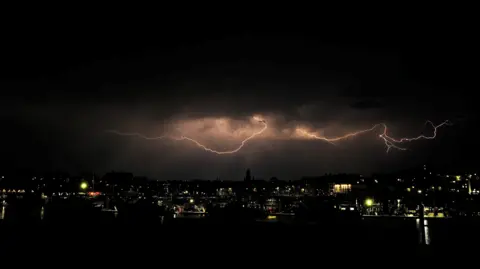 BBCWeatherWatchers/AstroMal A lightning strike seen emerging from the clouds above Ramsgate in Kent.