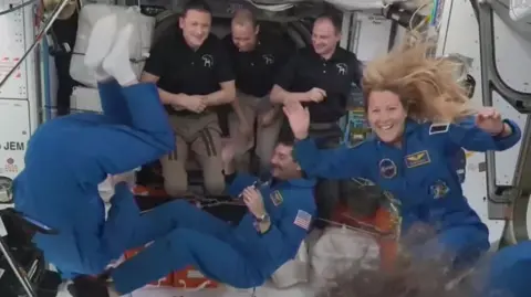 Astronauts floating about and waving onboard in the International Space Station