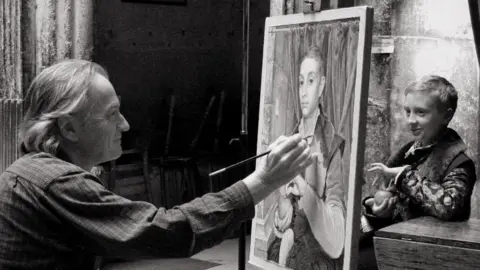 A black and white image of Michael Taylor painting Boy With Apple. Young Ed Munro is modelling for him.