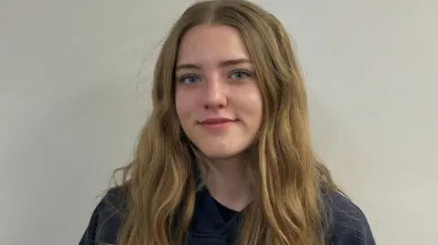 Supplied by Keegan Radomski An image showing Keegan Radomski. She has long slightly wavy blonde hair, blue eyes and is wearing a black shirt. Behind her is a plain, white backdrop. 