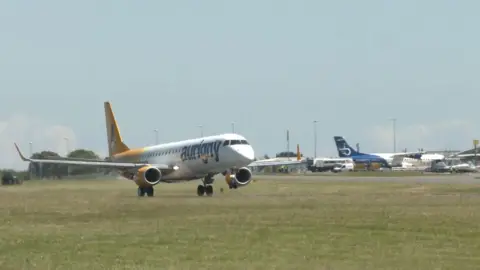 A white plane with jet engines with the word Aurigny on its nose taking off from Guernsey's airport runway.